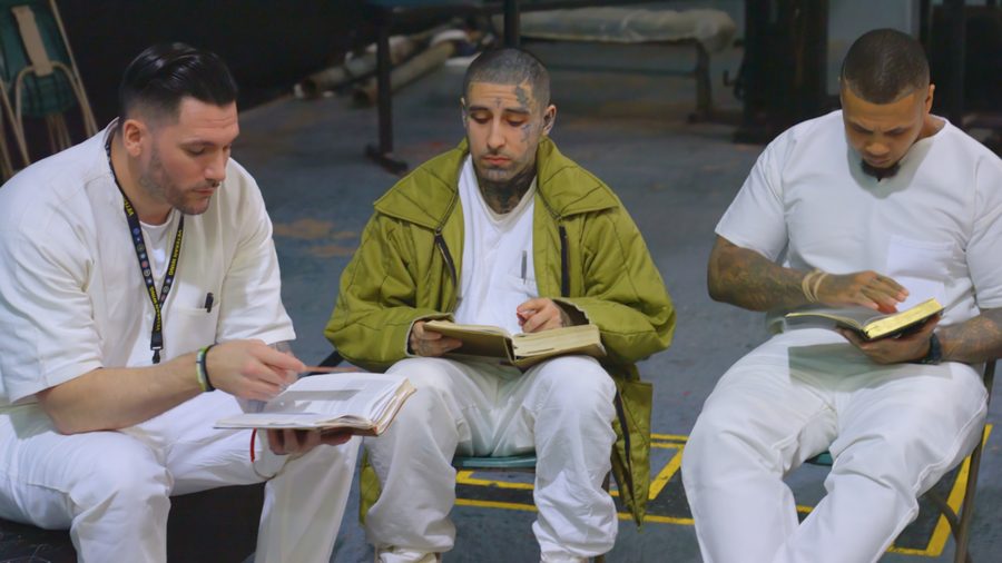 Three men in prison whites sitting together with open Bibles on their laps